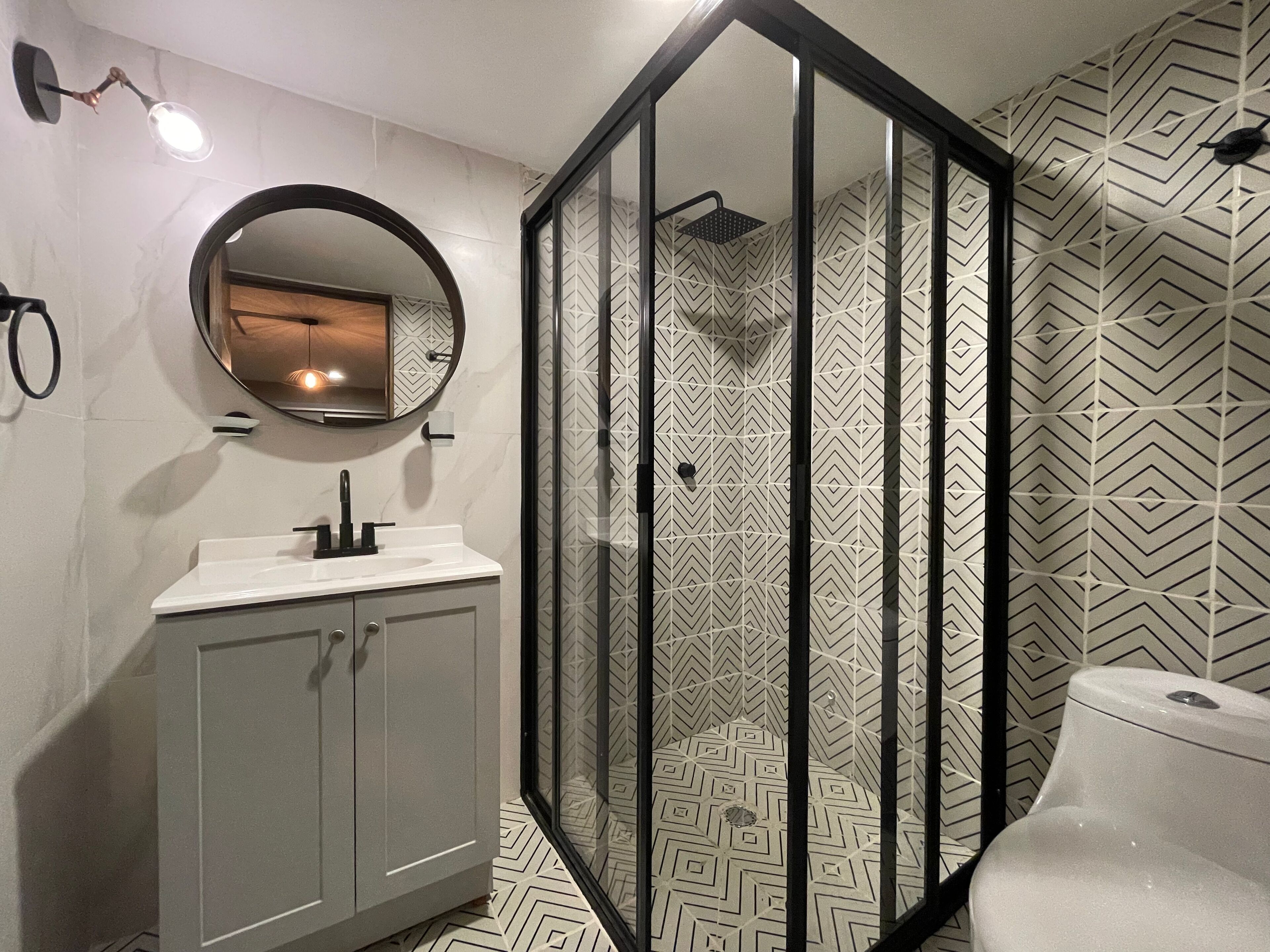 Ein modernes Badezimmer mit einer gläsernen Duschkabine, einem runden Spiegel und einem weißen Waschbecken.