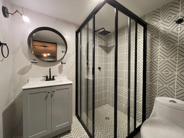 A modern bathroom with a glass-enclosed shower, a round mirror, and a white sink. - Estacion Alameda Downtown (Orizaba)
