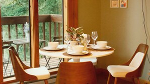 A dining area with a wooden table set for four, surrounded by chairs, and large windows offering a view of a wooden deck and greenery. - Rainier View Lodge - Mountain View Suite in Scenic Issaquah ｜ Seattle gateaway (Issaquah)