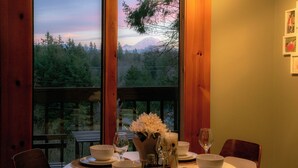 A dining table set with white bowls, wine glasses, and a candle centerpiece, overlooking a forested mountain landscape through large windows. - Rainier View Lodge - Mountain View Suite in Scenic Issaquah ｜ Seattle gateaway (Issaquah)