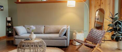 A cozy living room with a grey sofa, a wicker coffee table, a brown leather chair, and a large mirror.