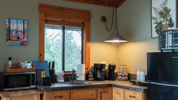 A kitchen with wooden cabinets, a black refrigerator, a coffee maker, and a window with blinds.