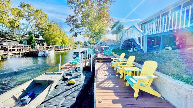 A dock with yellow chairs, a boat, and a building with blue railings. - Charming 2/2 waterfront farm home with tons of TV stations, WiFi, dock, & more (Spring Hill)