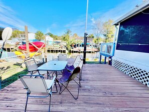 A wooden deck with outdoor seating, a view of a dock with boats, and a building with a screened porch. - Charming 2/2 waterfront farm home with tons of TV stations, WiFi, dock, & more (Spring Hill)