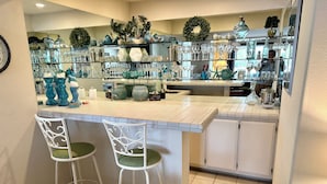 A bar area with two white bar stools, a tiled floor, and shelves stocked with glassware and decorative items.