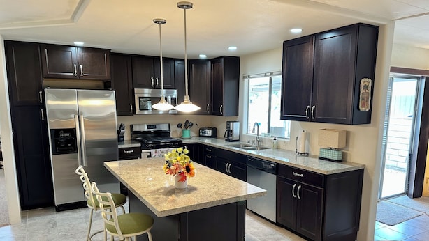 A modern kitchen with dark cabinetry, stainless steel appliances, a central island with a vase of flowers, and a window providing natural light.