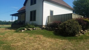 A two-story white house with a brown roof, a porch, and a stone wall with plants. - Charming Country farmhouse (Fredonia)