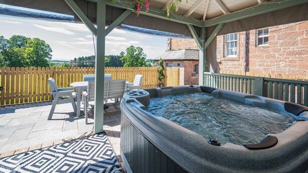 A covered outdoor area with a hot tub, chairs, and a patterned rug. - 3 bedroom accommodation in Annan (Annan)