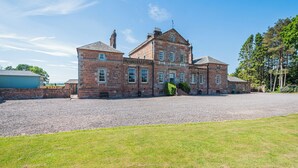 A large, historic stone building with multiple windows, a gravel driveway, and a grassy lawn. - 3 bedroom accommodation in Annan (Annan)