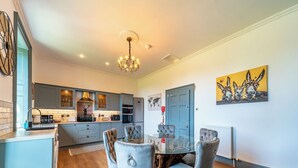 A modern kitchen with grey cabinets, a chandelier, and a dining area with grey upholstered chairs. - 3 bedroom accommodation in Annan (Annan)