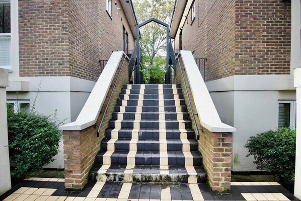 Stairs lead to an upper level, flanked by a brick wall and lush greenery.