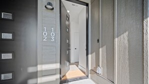 A modern hotel entrance with a dark door, a light-colored hallway, and a number display showing "102".