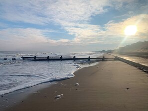 Uma praia com um calçadão de madeira, ondas e céu claro.