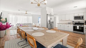 Een moderne keuken met roestvrijstalen apparatuur, een eethoek met een houten tafel en stoelen, en een woonkamer met een bank en gordijnen.