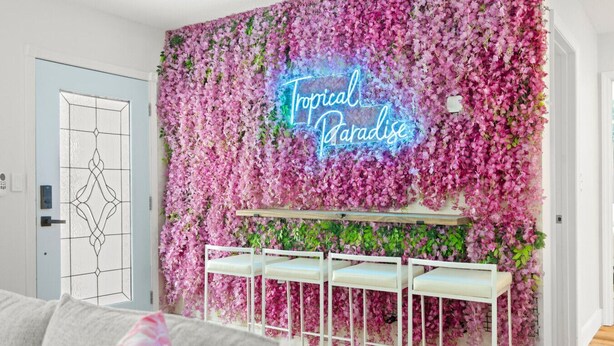 Een kamer met een muur bedekt met roze bloemen en een neonbord waarop staat: Tropical Paradise.