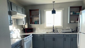 A modern kitchen with grey cabinets, a white stove, a black microwave, and a window above the sink.