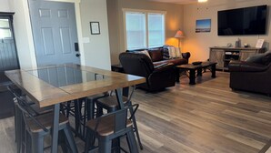 A modern living room with a glass-top dining table, leather sofas, and a flat-screen TV.