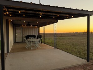 An outdoor patio with a table and chairs, a barbecue grill, and a view of a grassy field at sunset. - Fobb Getaway 3-BR house with WiFi, AC in Kingston area close to Lake Texoma (Kingston)