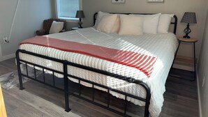 A bedroom with a bed, a TV mounted on the wall, two bedside tables with lamps, and a window with blinds.