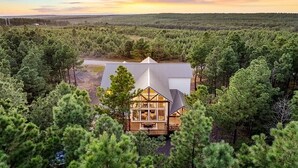 A cabin surrounded by dense forest with a large deck and a prominent chimney. - Diamond Sunset Retreat w/ Seasonal Pool, Hot Tub, Game Room & Outdoor Spaces! (Broken Bow)