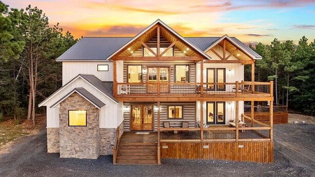 A two-story log cabin with a balcony and a stone foundation. - Diamond Sunset Retreat w/ Seasonal Pool, Hot Tub, Game Room & Outdoor Spaces! (Broken Bow)