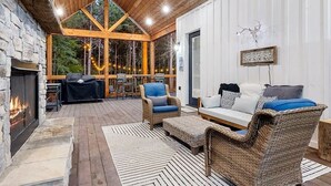 A cozy outdoor seating area with a stone fireplace, wicker furniture, and a view of the forest. - Diamond Sunset Retreat w/ Seasonal Pool, Hot Tub, Game Room & Outdoor Spaces! (Broken Bow)