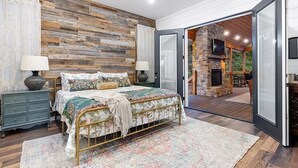 A bedroom with a large bed, a wooden wall, a TV, and a fireplace. - Diamond Sunset Retreat w/ Seasonal Pool, Hot Tub, Game Room & Outdoor Spaces! (Broken Bow)