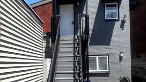 Un immeuble résidentiel à l’extérieur gris, avec un escalier métallique menant à une porte et une porte de garage.