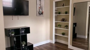 Une pièce dotée d’un téléviseur à écran plat fixé au mur, d’un plancher en bois et d’une porte blanche donnant sur une autre pièce.