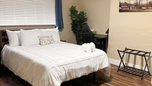 Une chambre avec un lit, un ventilateur de plafond, un climatiseur, un bureau avec une chaise, une plante et un plancher en bois.