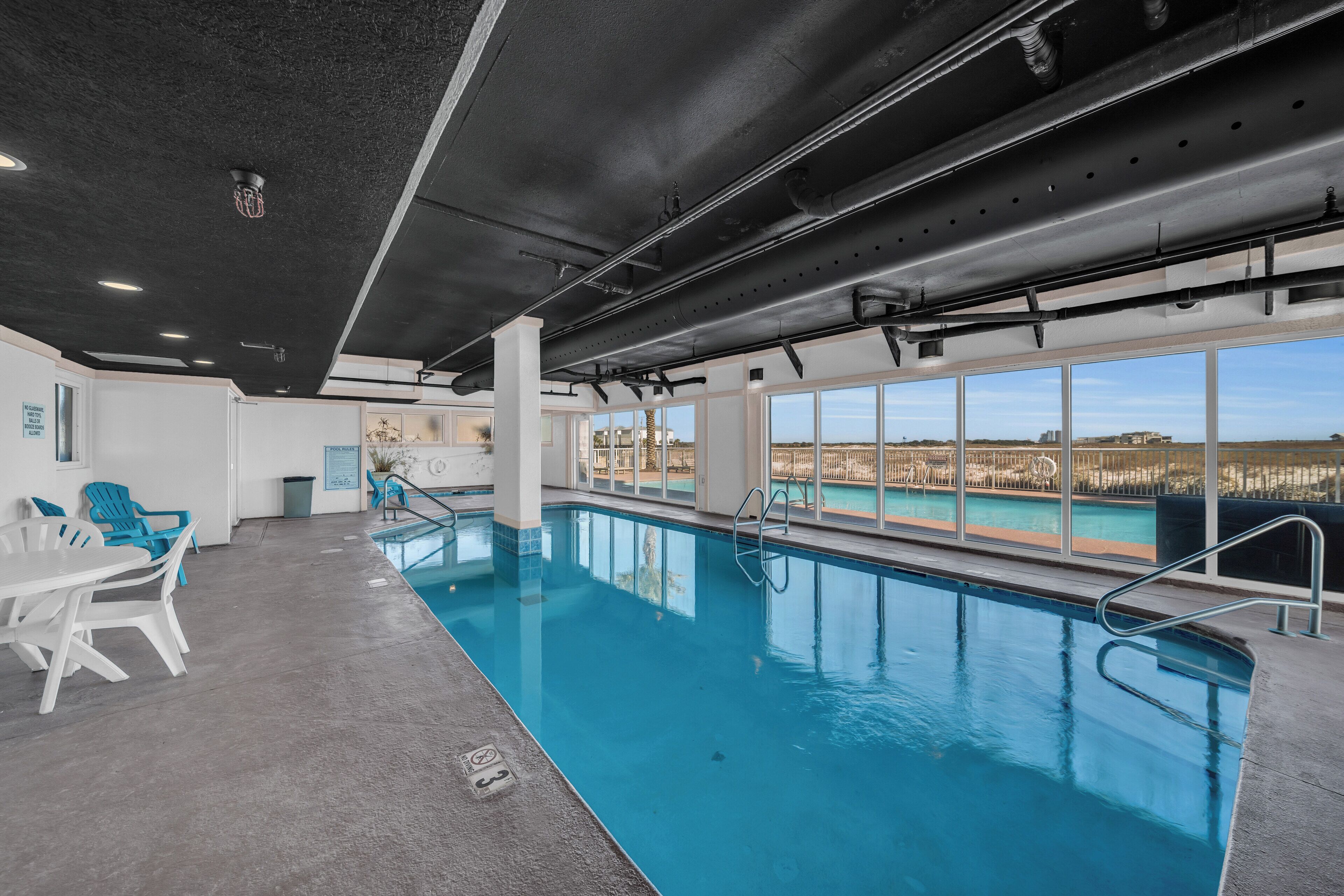 Una piscina interior con vistas despejadas al exterior, una zona de estar con sillones y un bar junto a la piscina.