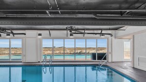 Une piscine intérieure avec de grandes baies vitrées, un escalier et une vue sur un paysage lointain.