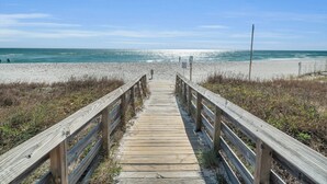 Une promenade en bois menant à une plage, avec un ciel dégagé.