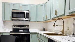 A compact kitchen with teal cabinets, stainless steel appliances, and a wooden floor. - The Cardinal 808 B - KING 1BR-1BA Apt
 (Evansville)