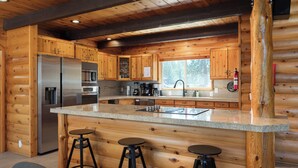 Eine Küchenlandschaft in einer Blockhütte mit Holzwänden, einem Edelstahlkühlschrank, einer Mikrowelle und einer großen Kochinsel mit Hockern.