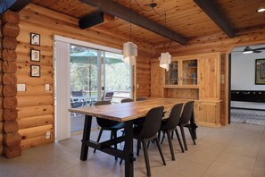 A wooden cabin interior with a dining table, chairs, a kitchen area, and a view through the glass door.
