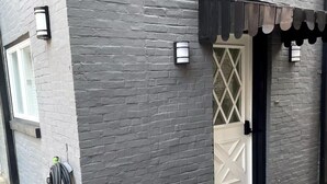 Un edificio con fachada de ladrillo gris, una puerta blanca con diseño de diamantes y un toldo negro sobre la puerta.