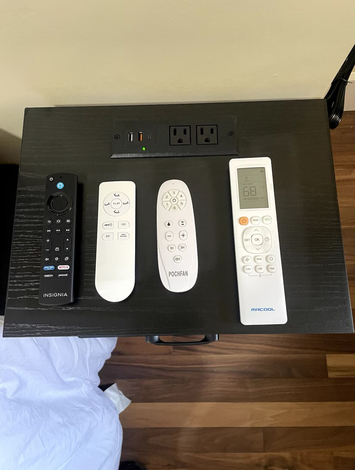 A black electronic device with multiple ports and a remote control on a wooden surface.