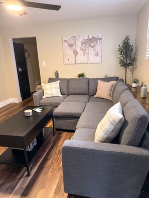 A modern living room with a sectional sofa, a dark coffee table, and a world map on the wall. - Iron City of South Side Flats Charming 2-bedroom Unit (Pittsburgh)