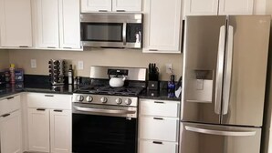 Una cocina con gabinetes blancos, un refrigerador de acero inoxidable, un microondas, una estufa y un horno empotrado.