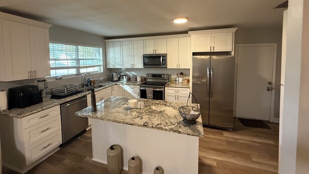 A modern kitchen with white cabinets, stainless steel appliances, and a marble countertop.