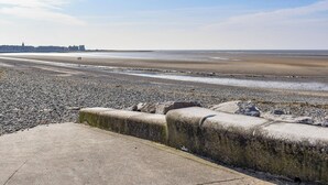 A wide, pebbly beach with a concrete barrier in the foreground.