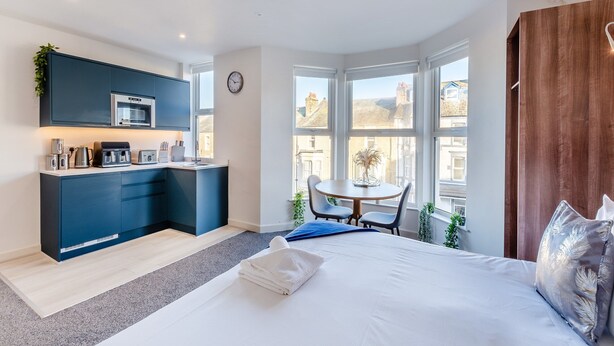 A modern hotel room with a kitchen, a dining area, and a large bed.
