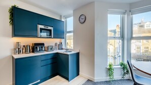 A modern kitchen with dark blue cabinets, a microwave, and a toaster. There is a window with a view of buildings outside.