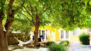 Un jardin avec un hamac, une maison jaune et un chemin de pierres.