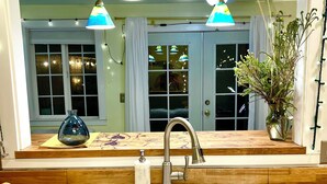Une cuisine dotée d’un évier à deux bacs, de luminaires suspendus, d’un vase avec des plantes et d’une fenêtre avec des rideaux.