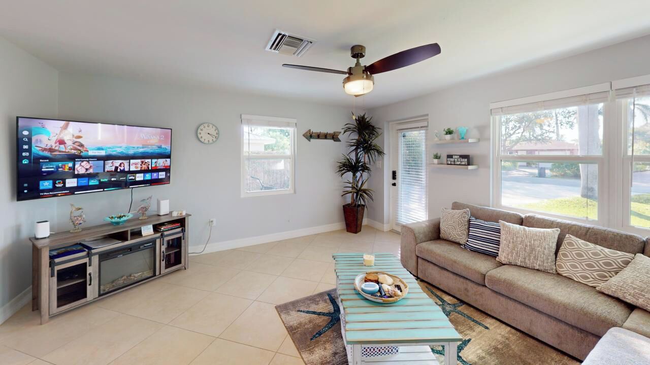 A living room with a flat-screen TV, a ceiling fan, a sofa, a coffee table, and a potted plant.