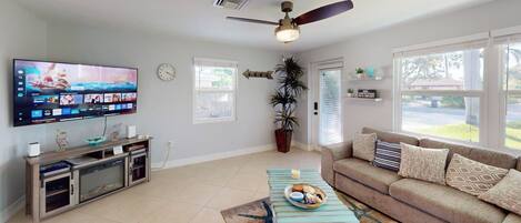 A living room with a flat-screen TV, a ceiling fan, a sofa, a coffee table, and a potted plant.