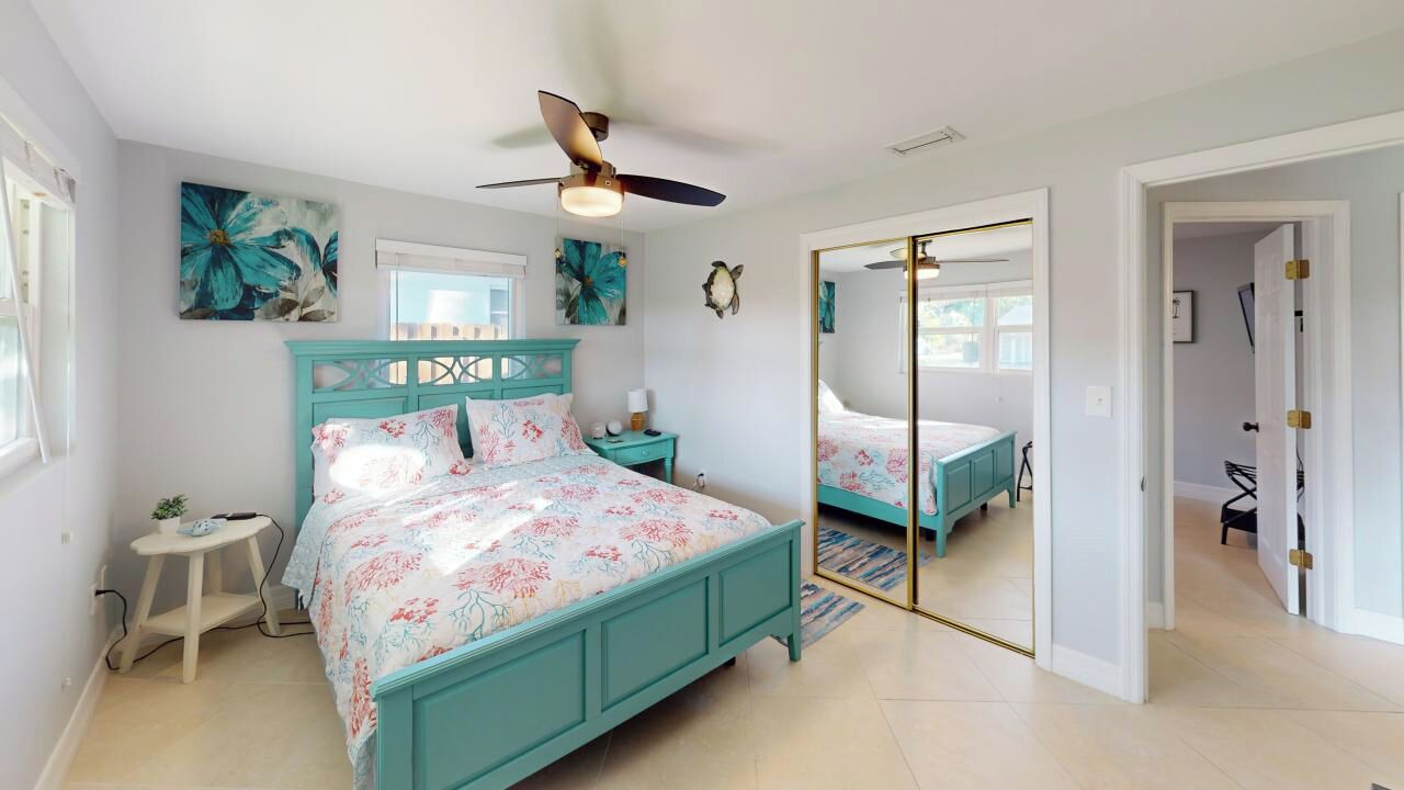 Une chambre à coucher avec un lit de couleur turquoise, une literie à motifs floraux, un ventilateur de plafond et un miroir.