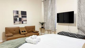 Une chambre d’hôtel avec un lit, un canapé en cuir marron, un téléviseur à écran plat, des rideaux à motifs et une œuvre d’art murale.